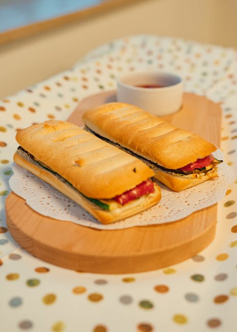 Two filled panini on a wooden board served with small dipping sauce