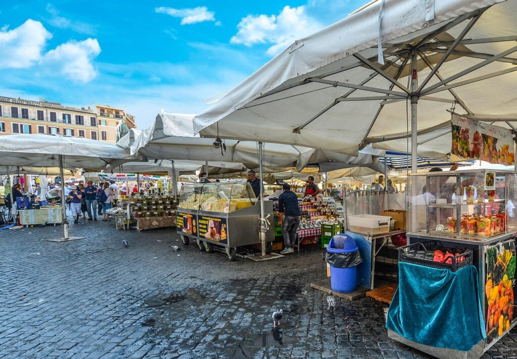 Outdoor market stalls with white canopies and customers on wet cobblestones