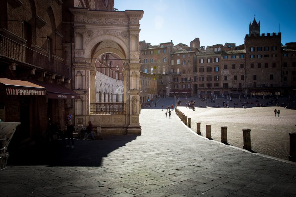 Sunlit Piazza del Campo in Siena with archway and scattered visitors