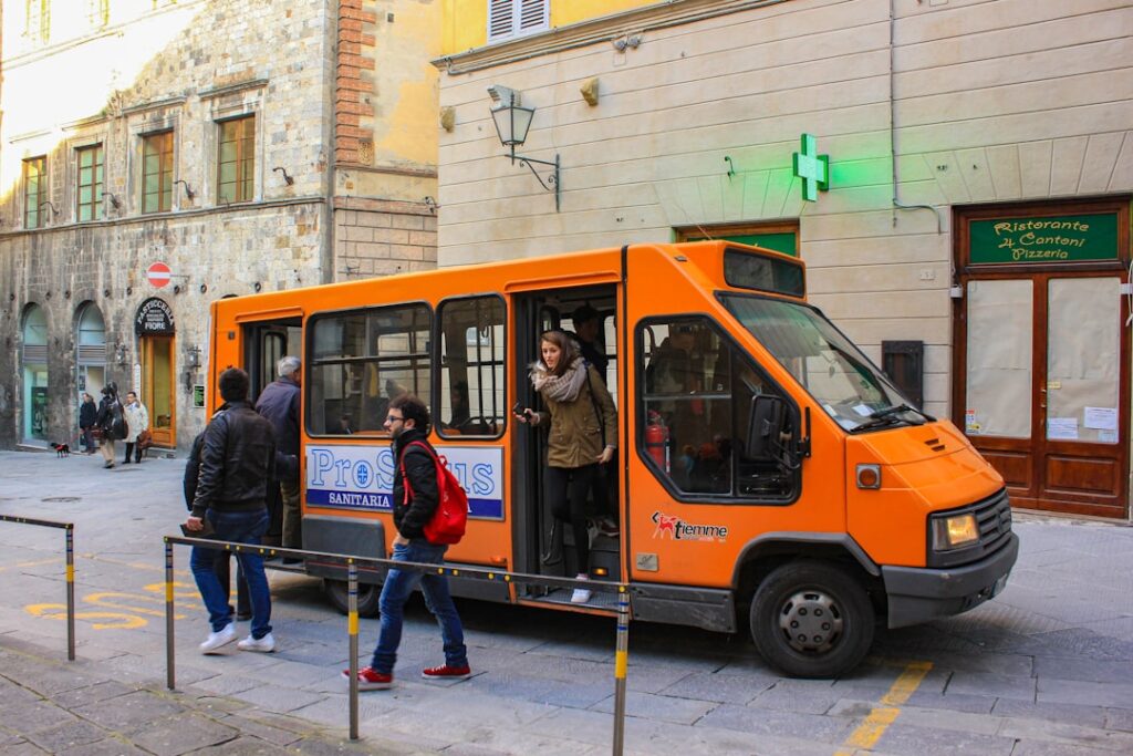 Orange city minibus stopping on a narrow street in Siena.