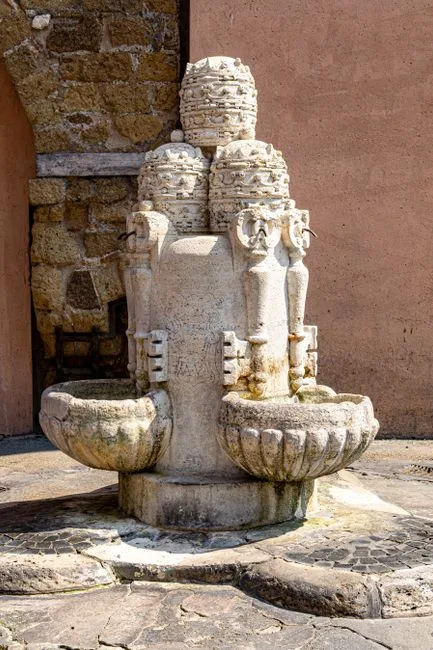 Fontaine en pierre sculptée avec bassins usés dans une petite place siennoise
