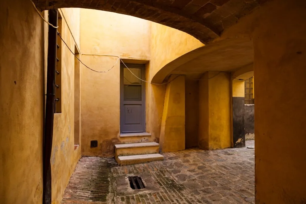 Cour intérieure aux murs jaunes sous une arche en pierre, ruelle de Sienne