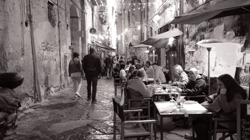 Ruelle étroite animée de clients attablés dans un restaurant de quartier à Sienne