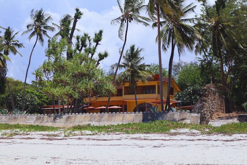 Strandvilla mit Palmen und gelbem Haus hinter Mauer auf Rhodos