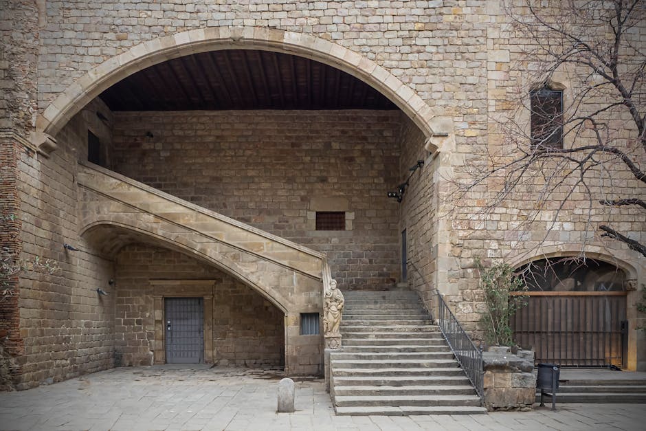 Arched stone courtyard with twin staircases and carved statue in Rhodes