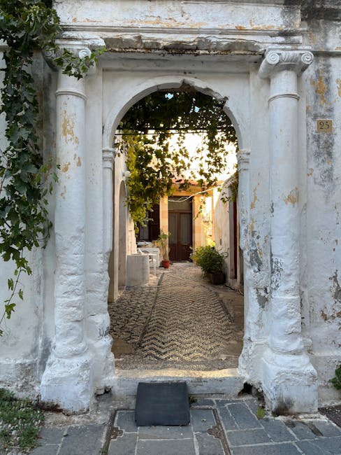 White arched entrance in Rhodes opening onto vine-covered pebble courtyard