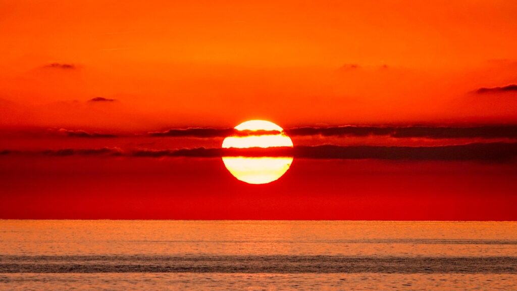 Feuerroter Sonnenuntergang über dem Meer bei Rhodos mit dunklen Wolkenstreifen