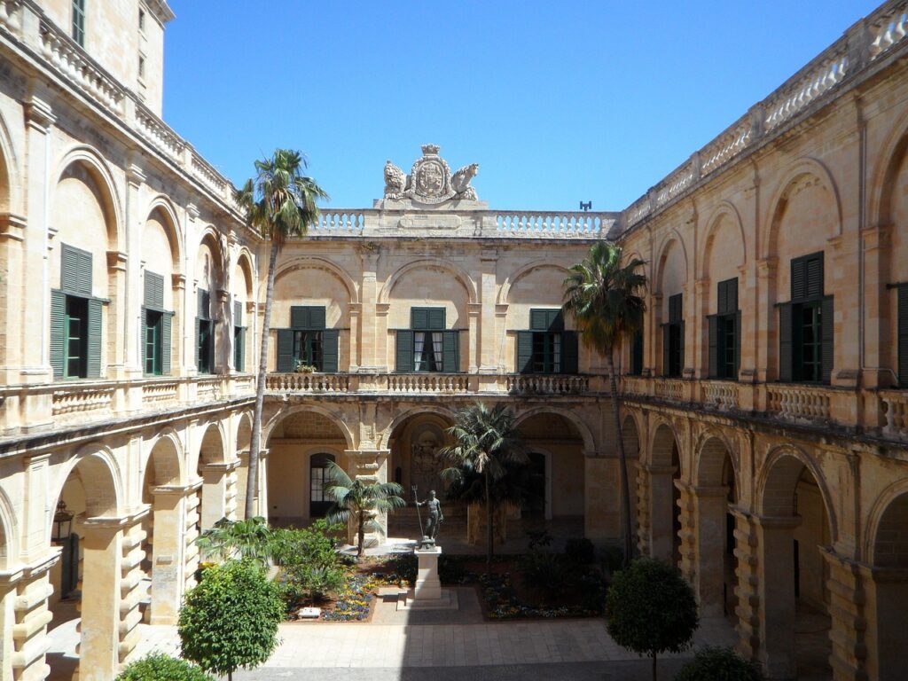 Chiostro soleggiato a Rodi con palme, statue e arcate doppie