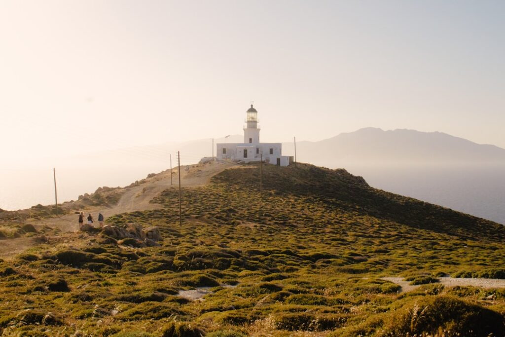 Phare blanc sur une colline herbeuse à Mykonos, visiteurs marchant