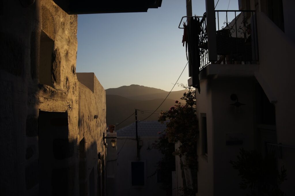 Schmale Gasse in Mykonos mit weißen Häusern und Sonnenuntergang hinter Bergen