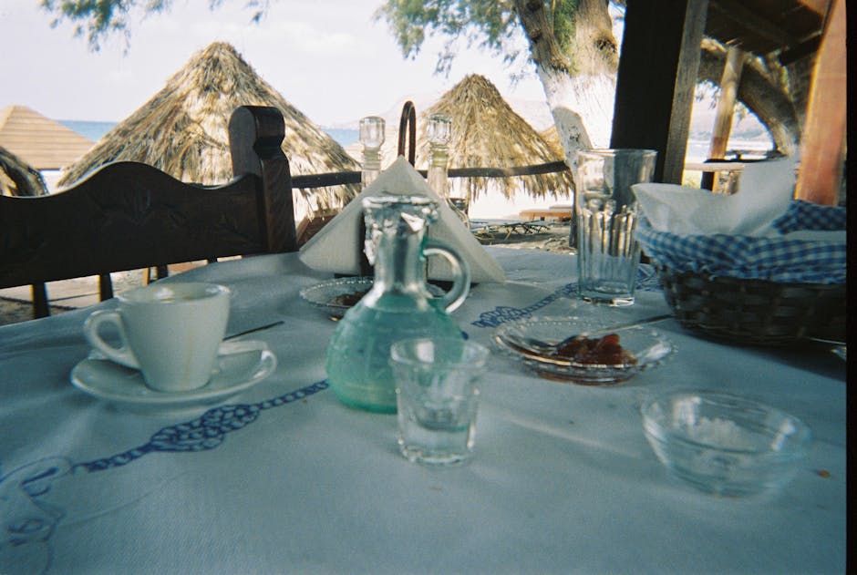 Tafel met koffie en karaf bij rieten parasols aan strand van Mykonos