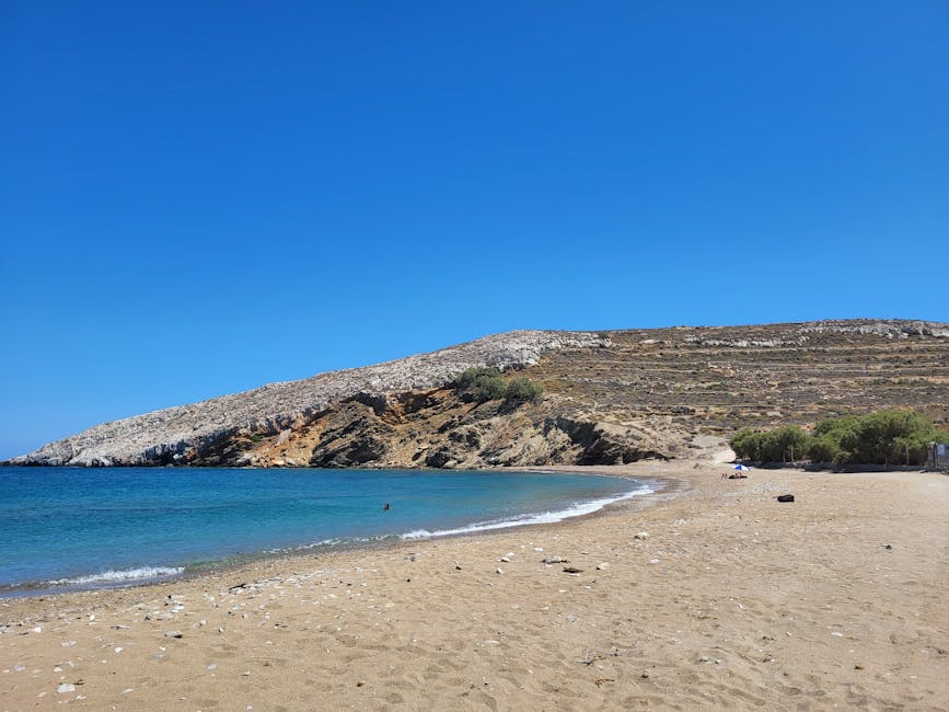 Lang rustig zandstrand met rotsachtige kaap en helder water op Mykonos