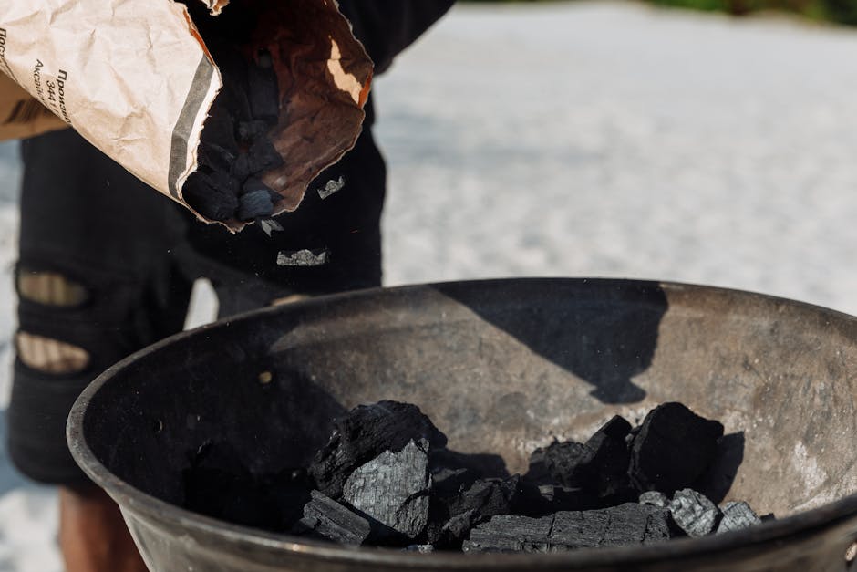 Personne versant charbon dans un barbecue portable sur la plage
