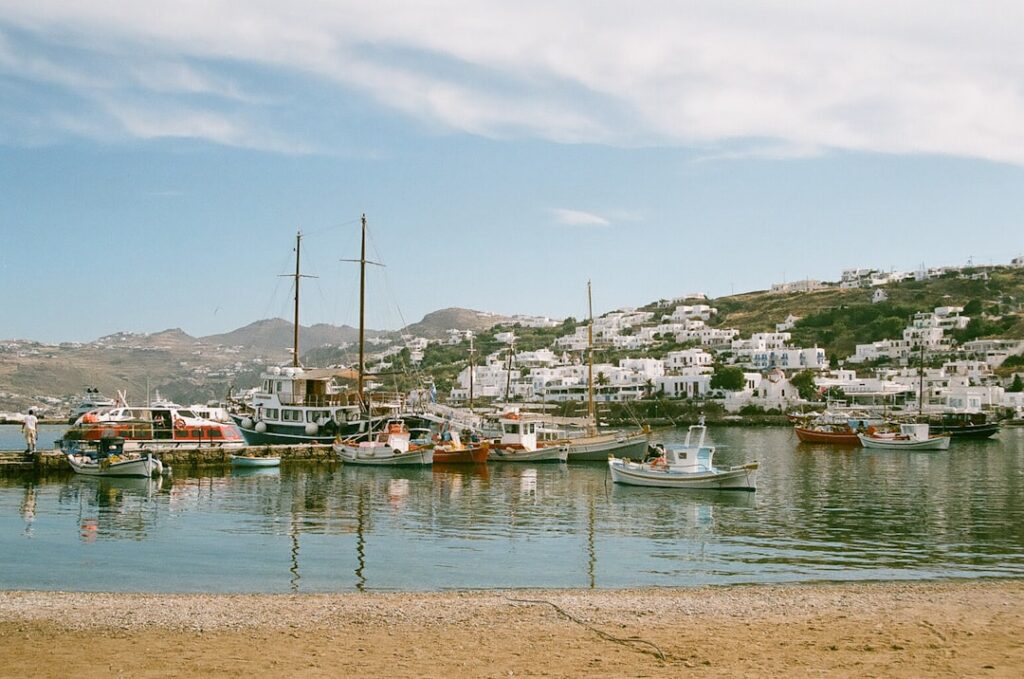 Kleine vissersbootjes aangemeerd in haven met witte huizen op heuvel Mykonos