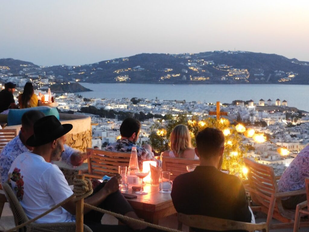 Terras met verlichte tafels en uitzicht op Mykonos stad en windmolens