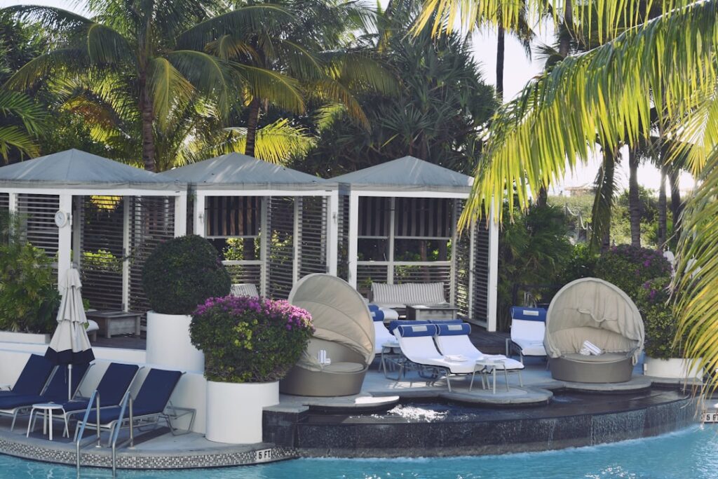 Cabanes et chaises longues autour d'une piscine bordée de palmiers.