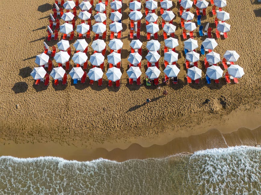 Bovenaanzicht rijen witte parasols en rode ligbedden op zandstrand Mykonos