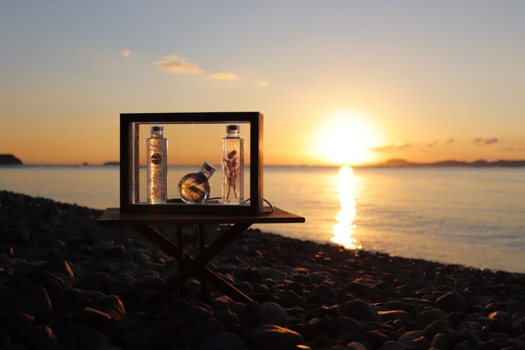 Cadre en verre posé sur galets avec fioles illuminées au coucher de soleil à Mykonos.