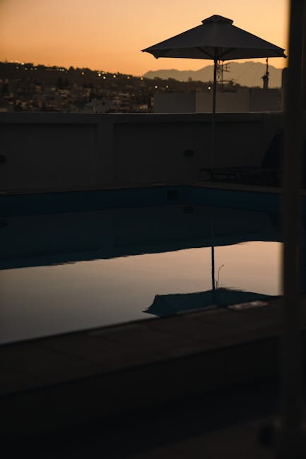 Umbrella silhouette reflected in still pool at Mykonos dusk.