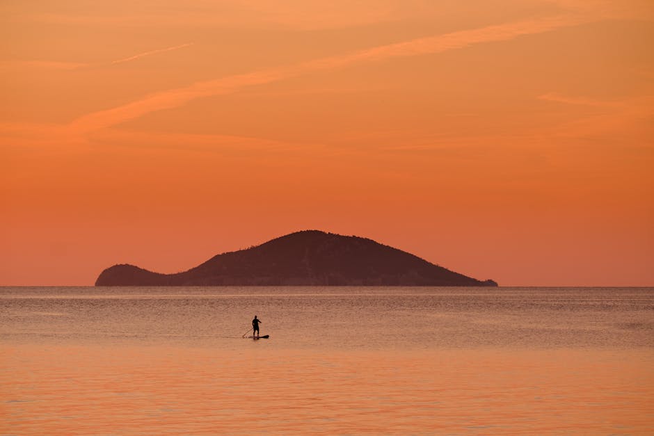 Paddleur solitaire naviguant devant un îlot orangé au large de Mykonos