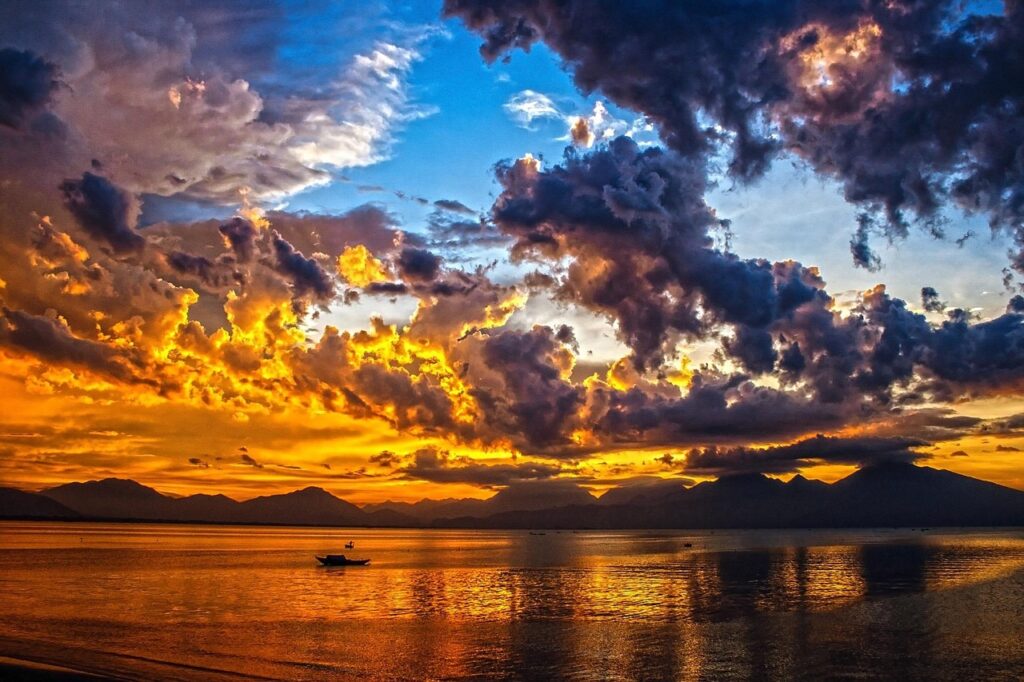 Vuurrode zonsondergang boven zee met bootje en bergen bij Mykonos