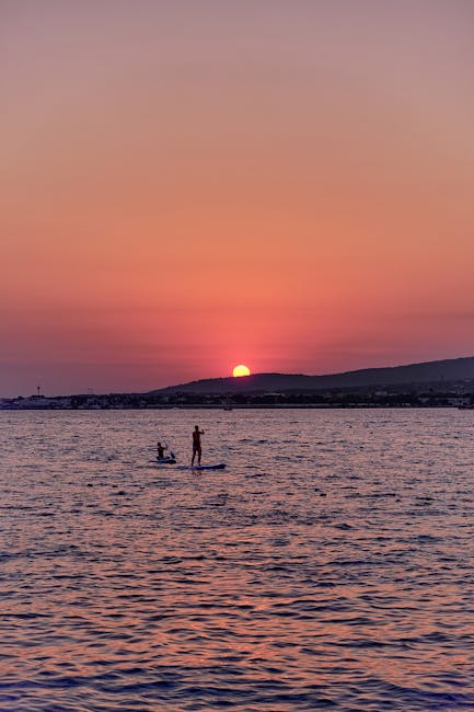 Deux pratiquants en paddle silhouettés devant le coucher de soleil à Mykonos