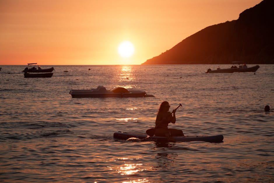 Personne en paddle agenouillée près d'embarcations, soleil couchant à Mykonos