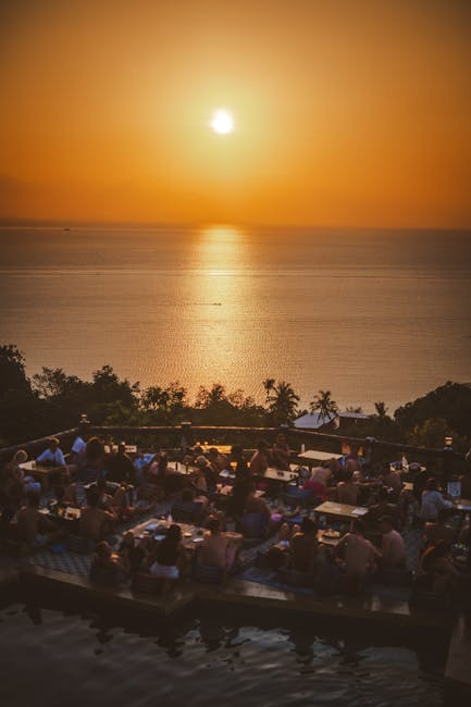 Publiek op terrassen kijkt naar gouden zonsondergang boven de zee