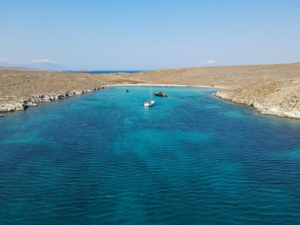 Turquoise secluded bay near Mykonos with anchored sailboats and beach