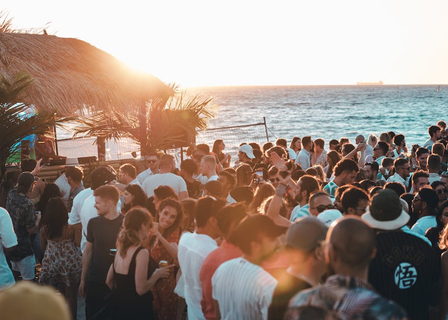 Foule festive au coucher de soleil sur plage de Mykonos, palmiers présents