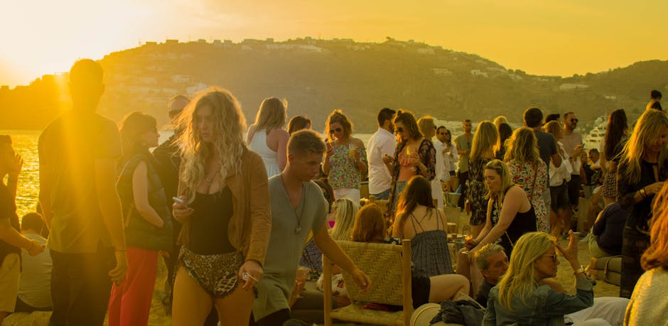 Drukke strandborrel met feestende mensen bij zonsondergang in Mykonos