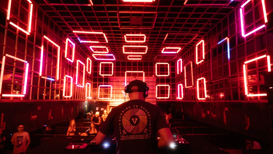 DJ casqué face au public, structure carrée de néons rouges à Mykonos