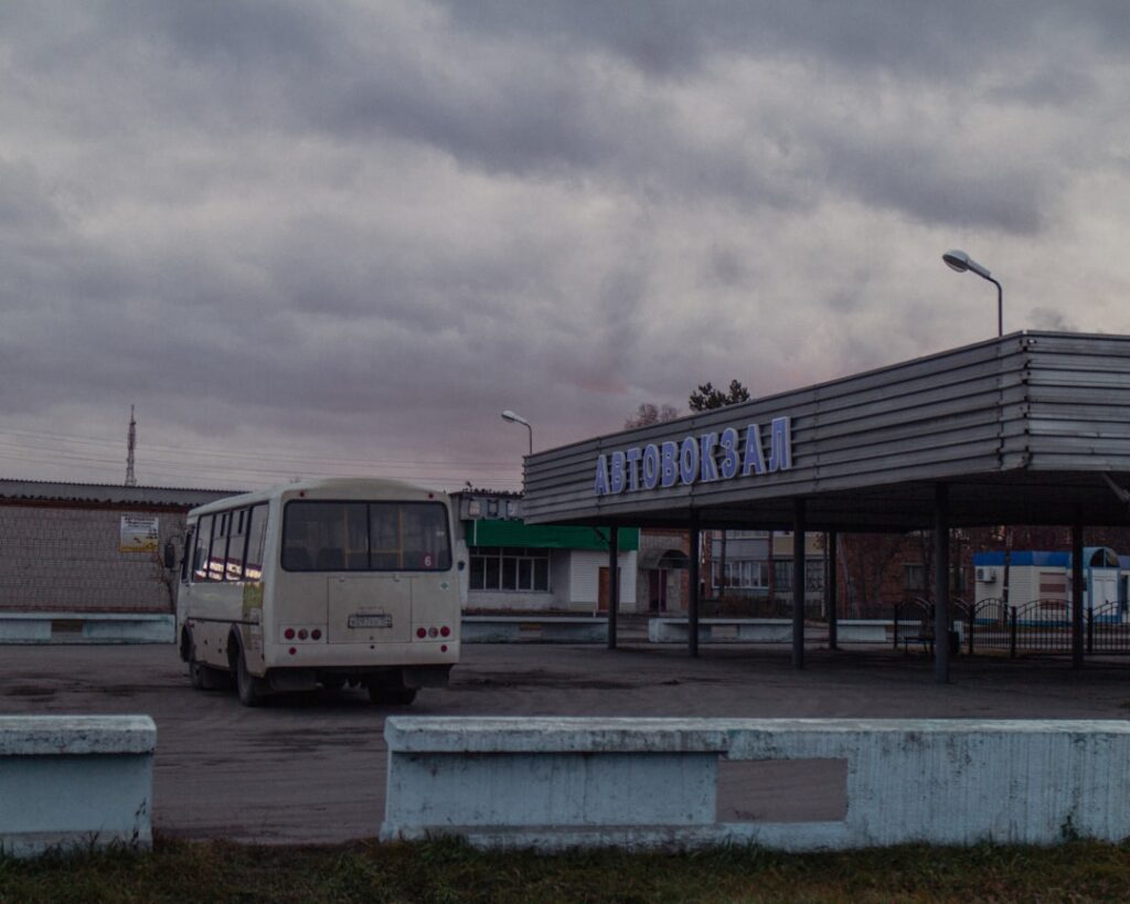 Empty bus parked outside a deserted bus station under cloudy sky