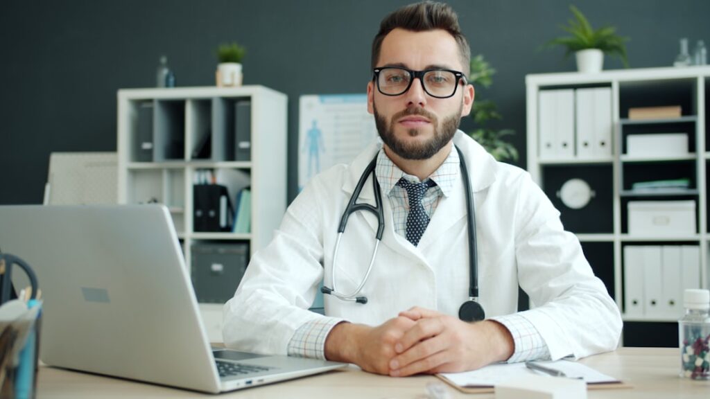 Medico nello studio con camice, stetoscopio e laptop davanti