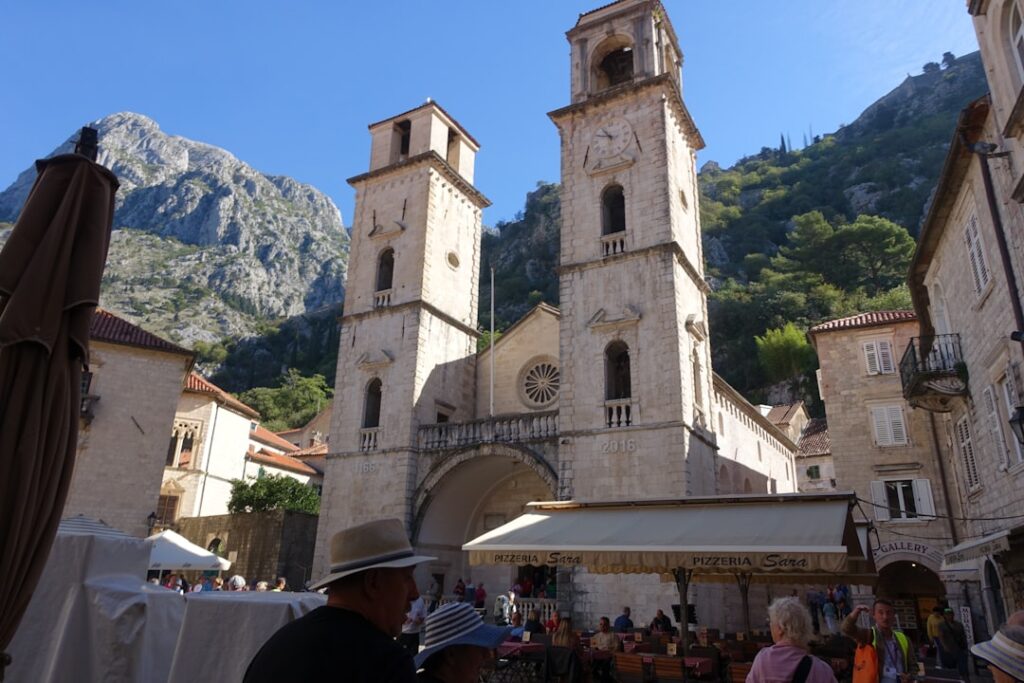 Kotor cathedral with twin bell towers overlooking busy outdoor cafés.