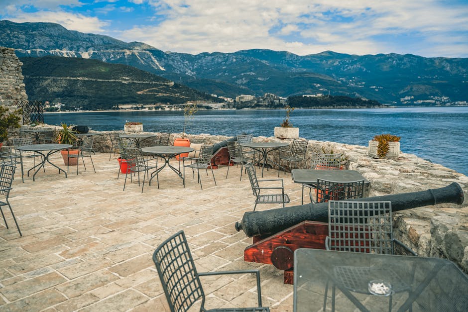 Outdoor terrace with metal tables and historic cannon overlooking Kotor Bay