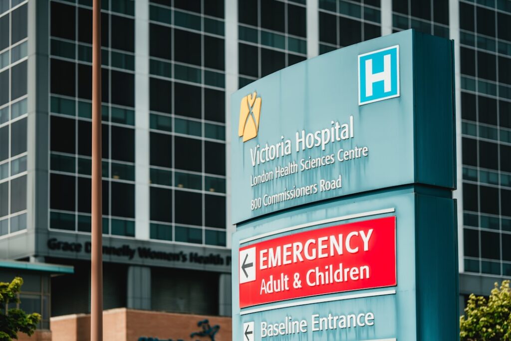 Krankenhausschild mit großem roten 'Emergency'-Schild vor Glasfassade
