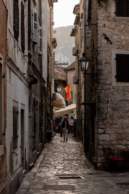 Narrow cobblestone Kotor alley with shutters and a Montenegrin flag.