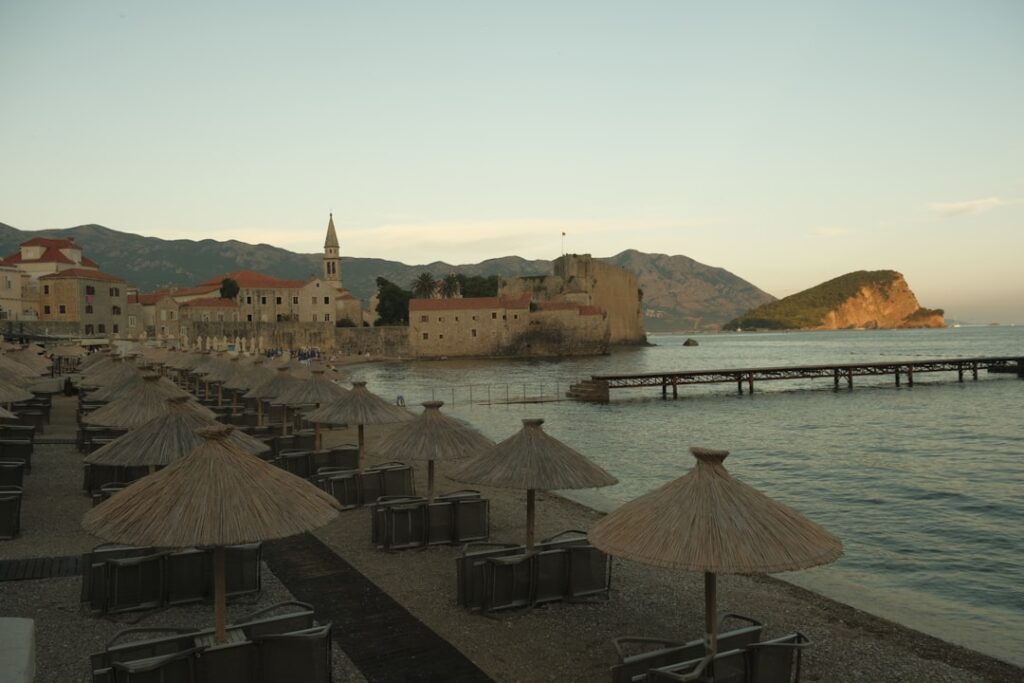 Ombrelloni di paglia sulla spiaggia con le mura antiche di Kotor sullo sfondo