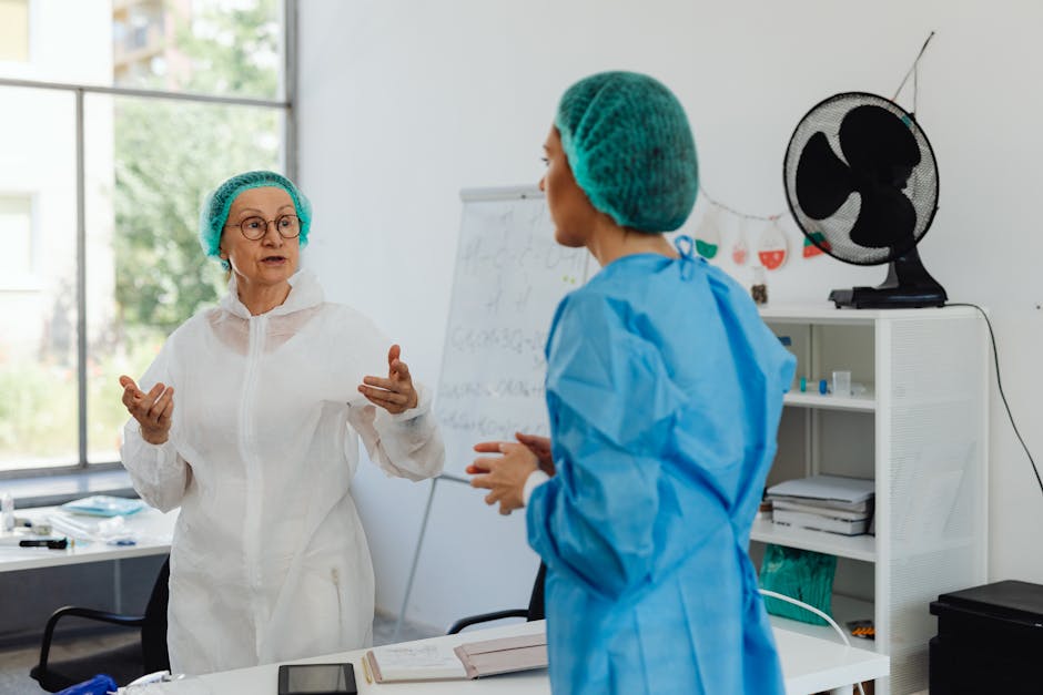 Zwei medizinische Mitarbeiterinnen in Schutzkleidung beraten sich im Behandlungsraum