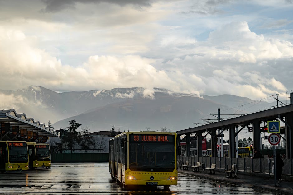 Gelber Bus am nassen Busbahnhof vor dramatischen Wolken und Bergen