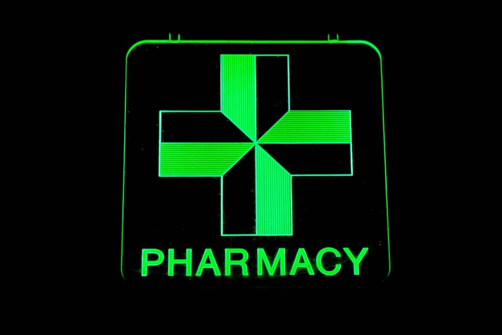 Glowing green pharmacy cross sign on black background