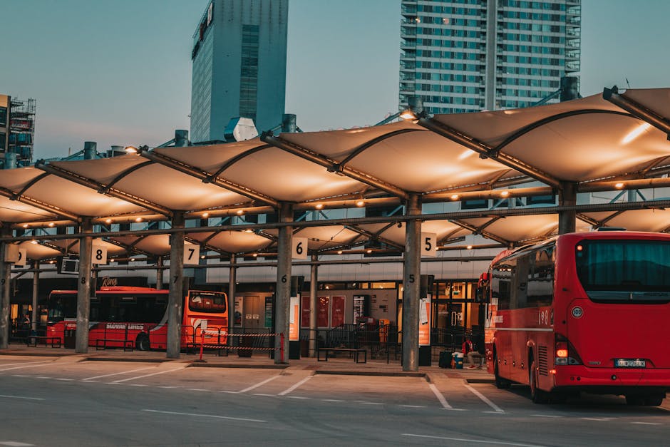 Covered bus terminal with numbered bays and red coaches at dusk