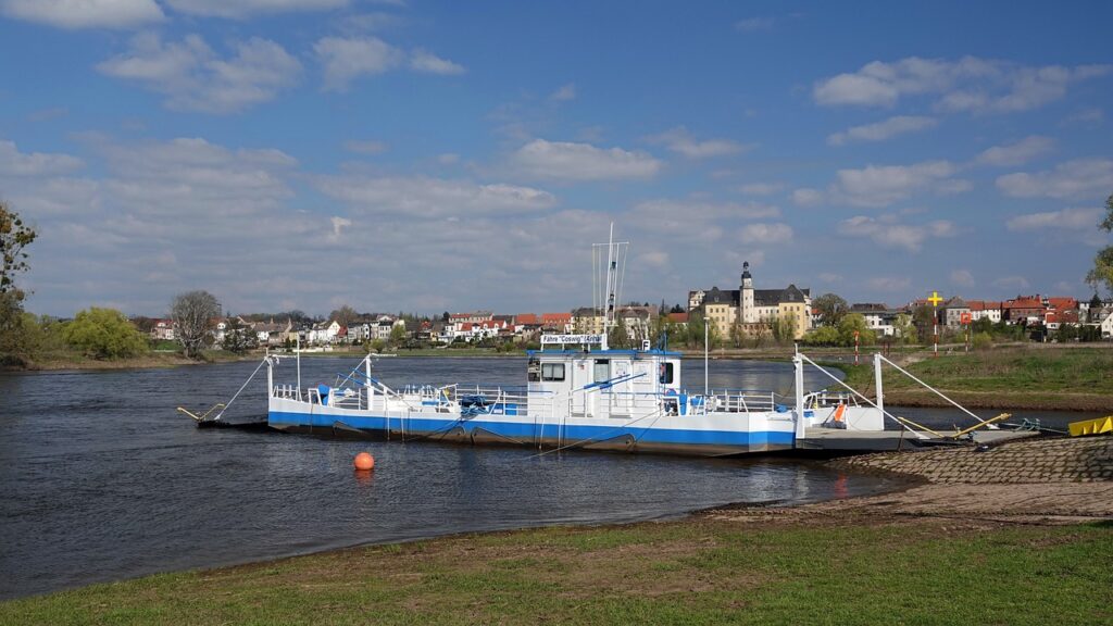 Kleine veerboot aan oever met dorp en rivier op achtergrond