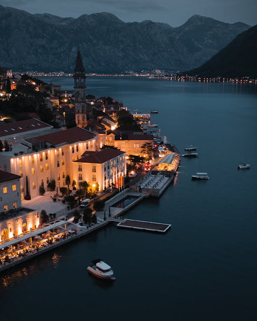 Kotor waterfront at dusk with lit buildings, docks, and moored boats
