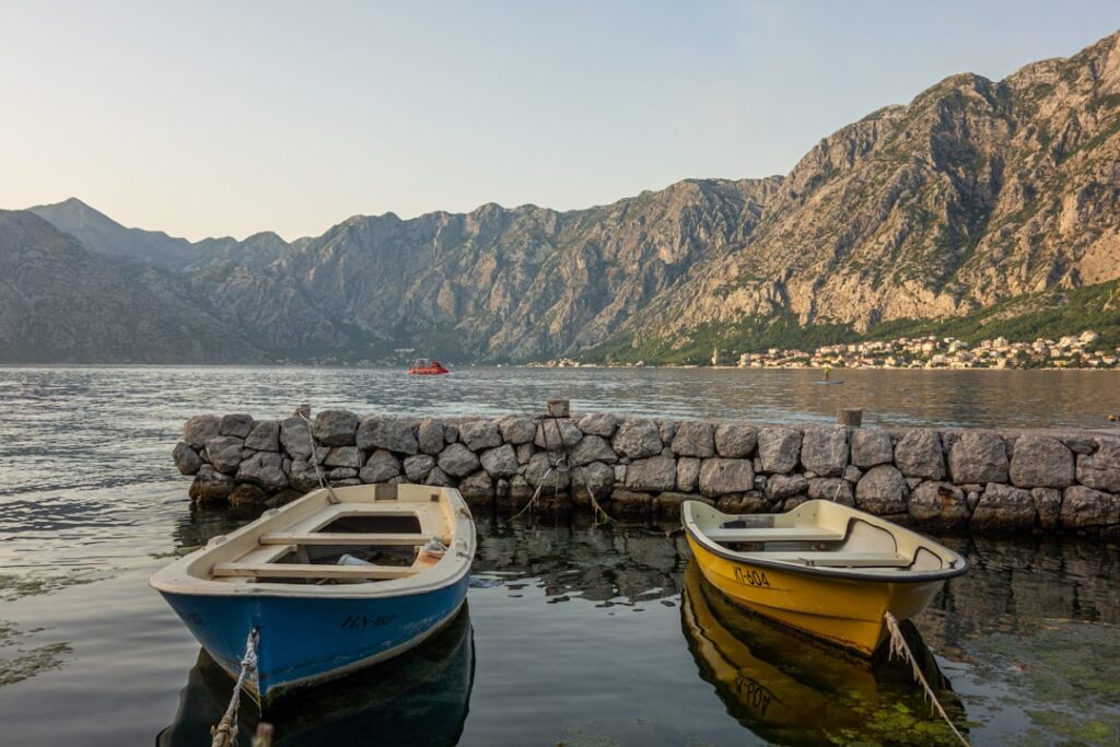 Due barche colorate attraccate al molo con montagne di Kotor