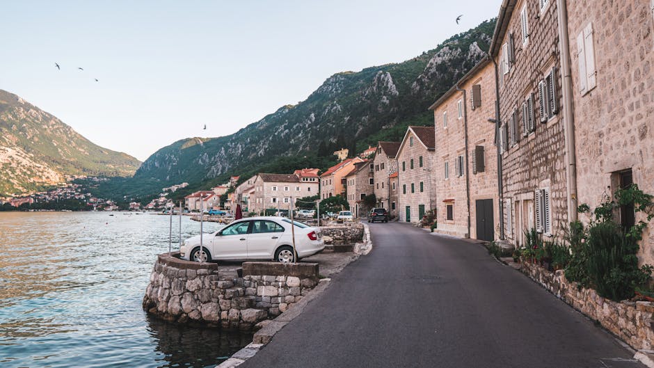 Narrow coastal road by Kotor's stone houses and parked cars along waterfront
