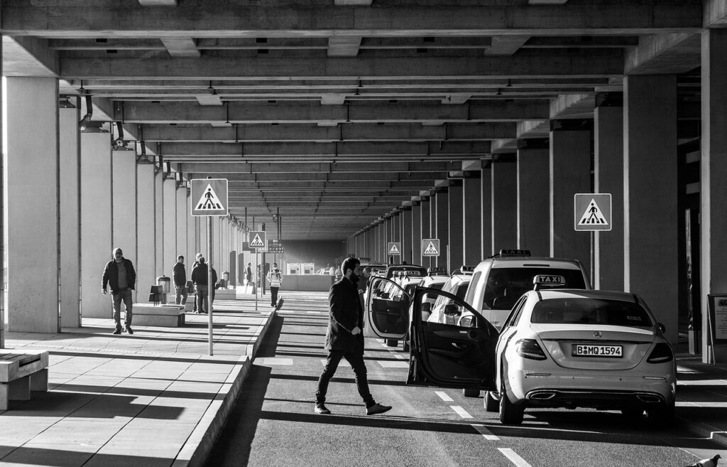 Taxiankunft unter Betonüberdachung mit wartenden Taxis und Fußgängern