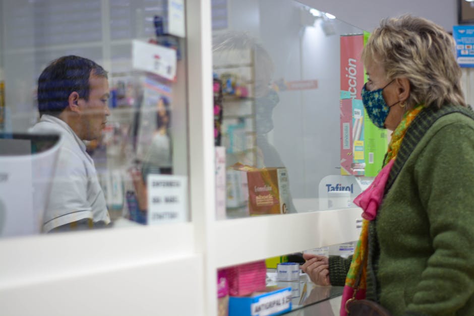 Klant met mondkapje praat via glazen afscheiding met apotheker in Kotor