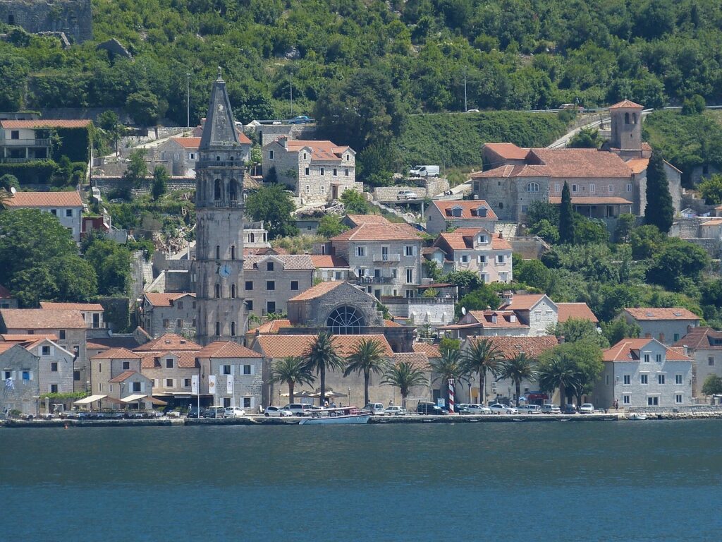 Uferort bei Kotor mit hohem Kirchturm und Palmen.